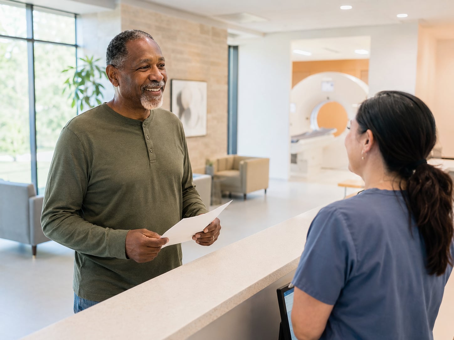 A man in scrub top holds a paper while talking with a female clinician