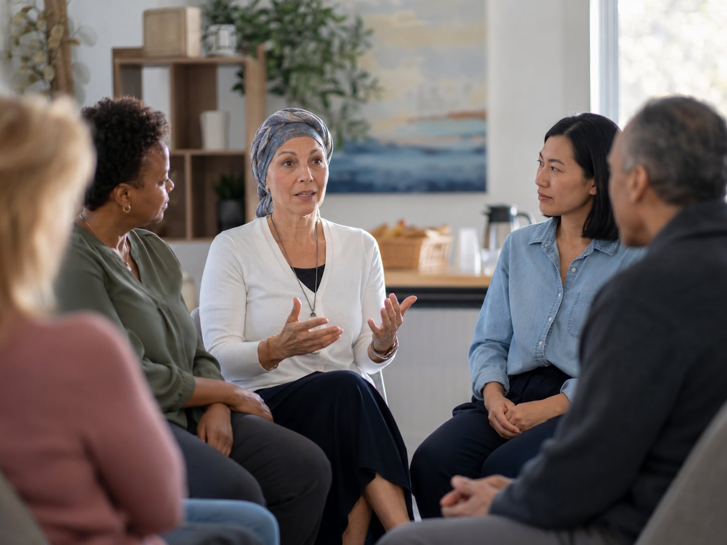 Three women sit together talking, one gesturing, in a living room