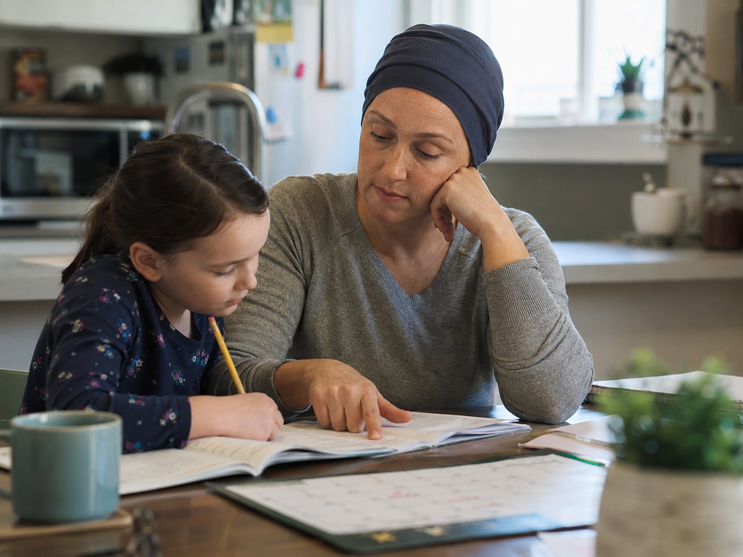 A woman in a headscarf helps a young girl with homework at the table