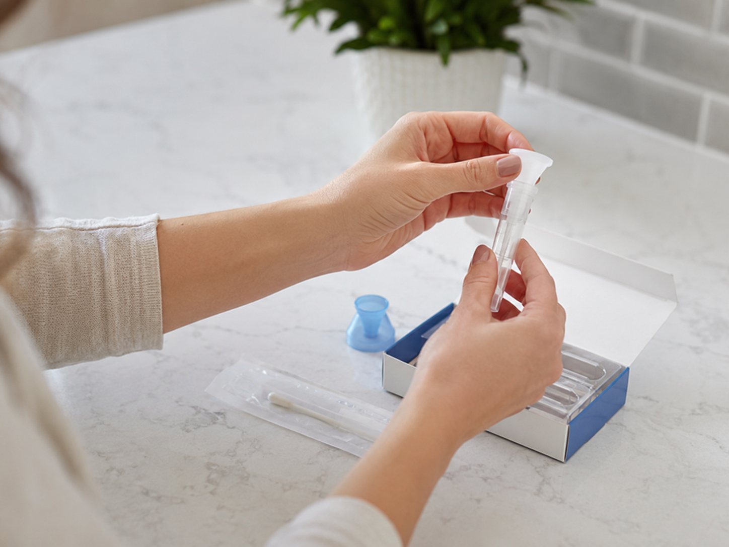 Hands lift a swab and tube from an at-home collection kit box on a kitchen counter