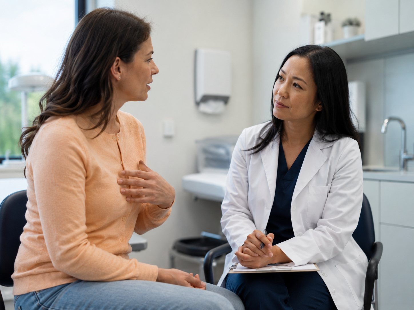 Woman gestures toward her chest while describing symptoms to a clinician taking notes in an exam room.