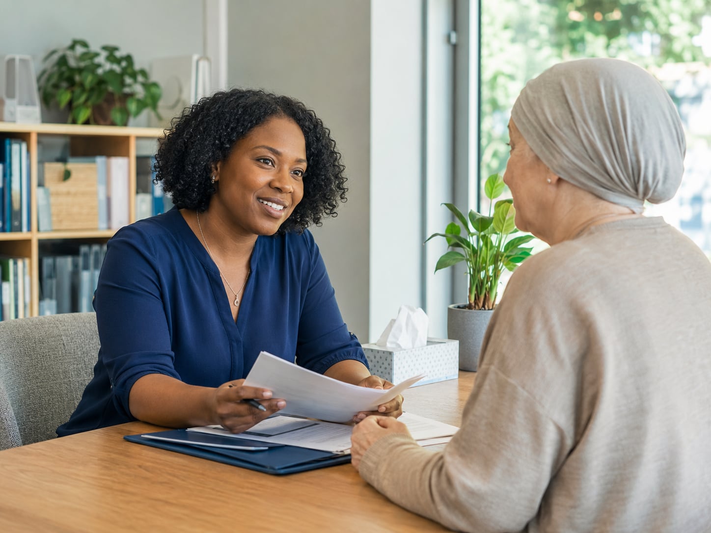 A female clinician hands a paper to an older woman wearing a headscarf at home